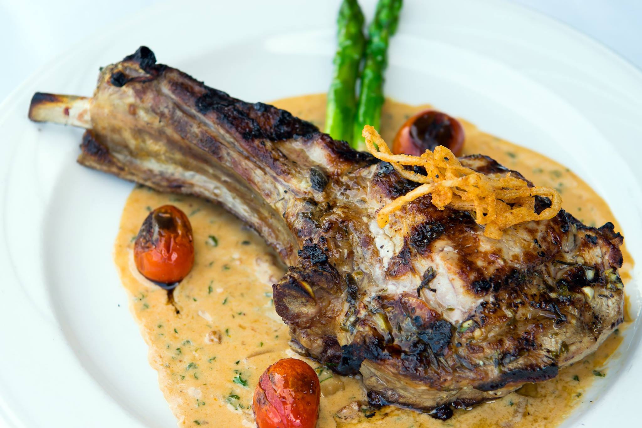 Grilled lamb chop served with creamy sauce, roasted cherry tomatoes, and asparagus